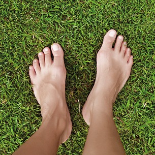 Bare feet standing on green and wealthy grass to symbolize the minimization of the ecological footprint.